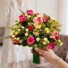 Beautifully layered with dense green ferns, broad-leaf foliage, and petite ivory buds.